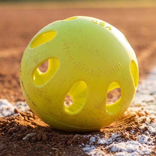 Yellow-green Stee-Rike 3 practice softball on baseball field dirt at base line